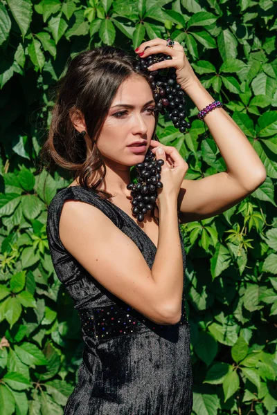 Portret van de jonge sexy brunette bijten zwart druiven. — Stockfoto