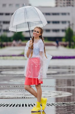 Genç güzel kız sarı çizmeli iki örgüler ve şeffaf şemsiye standları Çeşme yakınındaki.