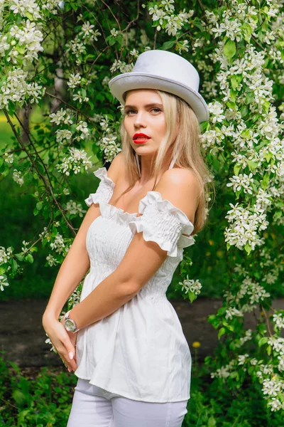Sexy moderne bruid in witte cilinder hoed enjoing bloomin apple boom bloemen. — Stockfoto