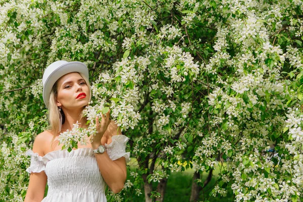 Sexy moderne bruid in witte cilinder hoed enjoing bloomin apple boom bloemen. — Stockfoto