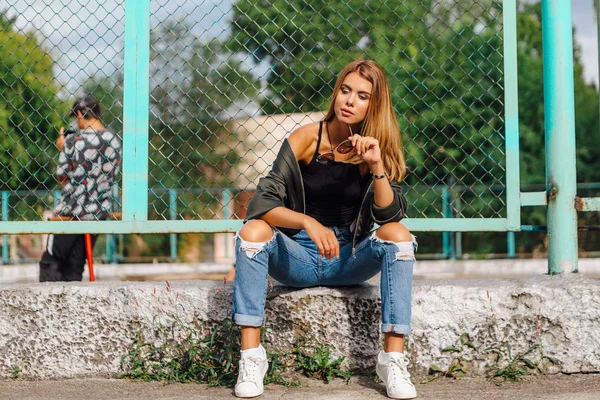 Модный портрет модной молодой женщины в солнцезащитных очках и пиджак подрывника, сидящего рядом с Рабицем в городе — стоковое фото