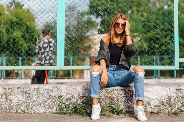 Retrato de moda de una joven de moda con gafas de sol, y chaqueta de bombardero sentado junto a Rabitz en la ciudad — Foto de Stock