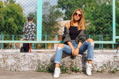 Güneş gözlüğü ve sıva şehrin yanında oturan bombardıman ceket giyen trendy genç kadın moda portre