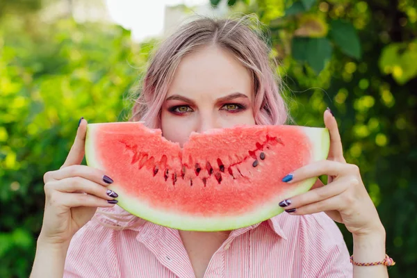 Beautiful young woman with pink hair holding juicy watermelon close to the face — Stock Photo, Image