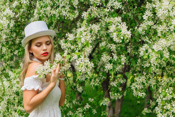 Sexy moderne bruid in witte cilinder hoed enjoing bloomin apple boom bloemen. — Stockfoto