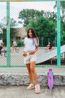 Yaz yaşam tarzı görüntü trendy genç ve güzel kız onun plastik scateboard ile scateboard coart yanında ayakta.