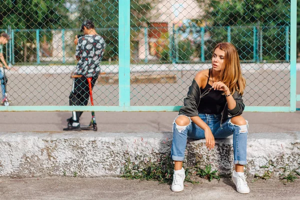 Fashion portrait of trendy young woman wearing sunglasses, and bomber jacket sitting next to rabitz in the city — Stock Photo, Image