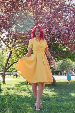 Sarı giysili bir çiçek açan bir elma ağacı yanında duran parlak kırmızı saç ve ref dudaklar ile güzel ve genç kadın.