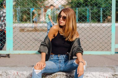 Güneş gözlüğü ve sıva şehrin yanında oturan bombardıman ceket giyen trendy genç kadın moda portre