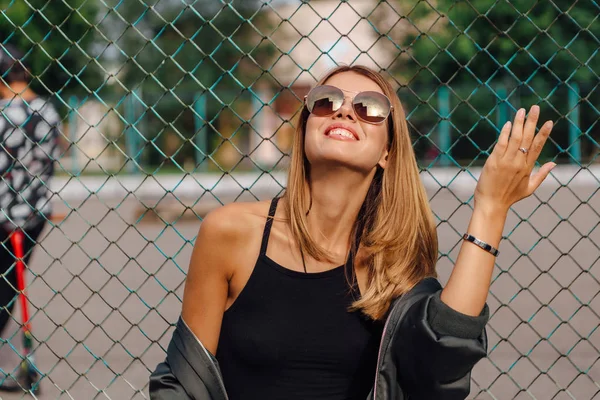 Retrato de moda de jovem na moda usando óculos de sol, e jaqueta de bombardeiro sentado ao lado de rabitz na cidade — Fotografia de Stock