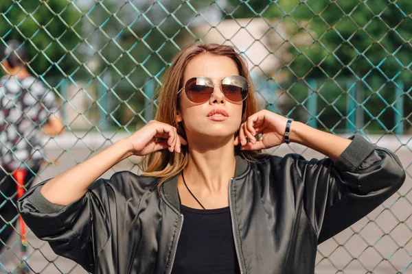 Mode porträtt av trendiga ung kvinna som bär solglasögon och bombplan jacka sitter bredvid rabitz i staden — Stockfoto