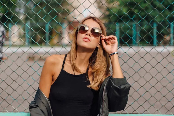 Retrato de moda de jovem na moda usando óculos de sol, e jaqueta de bombardeiro sentado ao lado de rabitz na cidade — Fotografia de Stock