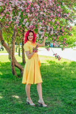 Sarı giysili bir çiçek açan bir elma ağacı yanında duran parlak kırmızı saç ve ref dudaklar ile güzel ve genç kadın.