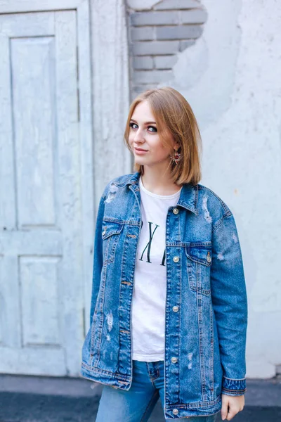 Chica de moda de pie cerca de la pared de ladrillo en chaqueta de mezclilla y hermosos pendientes . — Foto de Stock