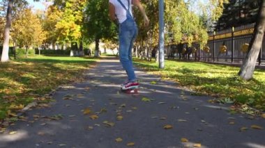 Kot overolls genç kadın sonbahar yolda pembe tekerlekler ile mavi plastik kaykay sürmek.