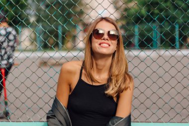 Güneş gözlüğü ve sıva şehrin yanında oturan bombardıman ceket giyen trendy genç kadın moda portre