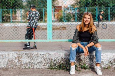 Güneş gözlüğü ve sıva şehrin yanında oturan bombardıman ceket giyen trendy genç kadın moda portre