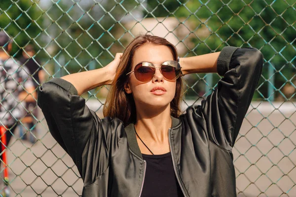 Retrato de moda de jovem na moda usando óculos de sol, e jaqueta de bombardeiro sentado ao lado de rabitz na cidade — Fotografia de Stock