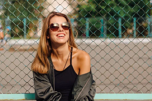 Retrato de moda de jovem na moda usando óculos de sol, e jaqueta de bombardeiro sentado ao lado de rabitz na cidade — Fotografia de Stock