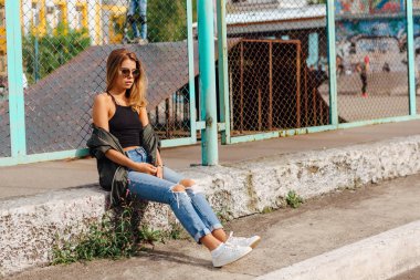 Güneş gözlüğü ve sıva şehrin yanında oturan bombardıman ceket giyen trendy genç kadın moda portre