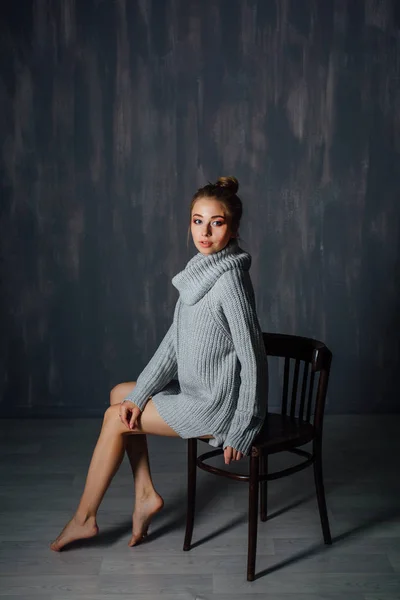 Πορτρέτο της όμορφη νεαρή γυναίκα που κάθεται στην καρέκλα ντυμένος σε άνετο πλεκτό πουλόβερ. — Φωτογραφία Αρχείου