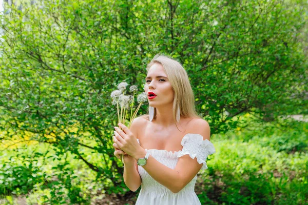 Beautiful blonde woman blowing on white blowball — Stock Photo, Image