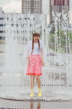 Sarı çizmeli genç, ıslak güzel kız çeşmenin içinde duruyor..