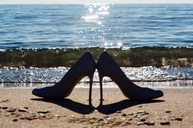 Deniz arka plan ile sahilde yüksek topuk kadın ayakkabı siyah siluet.
