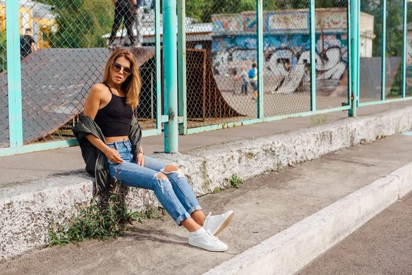Portrait de mode de jeune femme branchée portant des lunettes de soleil, et veste de bombardier assis à côté de rabitz dans la ville — Photo
