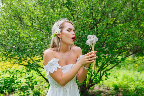 Beautiful blonde woman blowing on white blowball — Stock Photo, Image