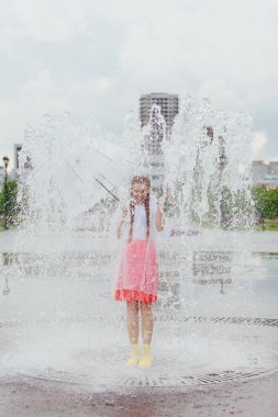 Sarı çizmeli ve fıskiyenin içinde şeffaf şemsiyeli iki örgülü genç ve güzel kız..