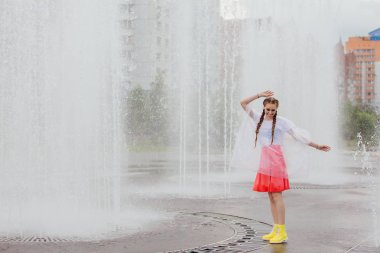 Sarı çizmeli iki örgülü genç, ıslak güzel kız çeşmenin yanında duruyor..