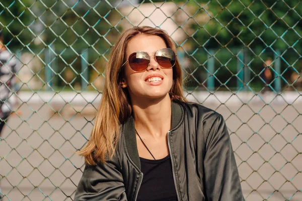 Mode porträtt av trendiga ung kvinna som bär solglasögon och bombplan jacka sitter bredvid rabitz i staden — Stockfoto