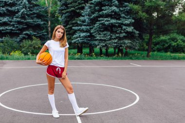 Güzel genç kız beyaz tişört, şort ve spor ayakkabısı, giyinmiş bir basketbol sahası üzerinde bir top ile çalış.