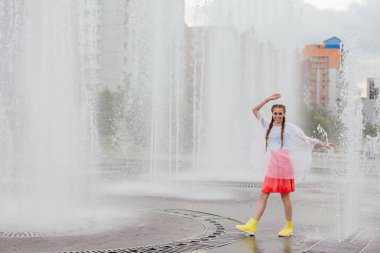 Sarı çizmeli iki örgülü genç, ıslak güzel kız çeşmenin yanında duruyor..