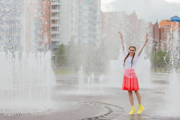 Gadis cantik basah muda dengan dua kepang sepatu kuning berdiri di dekat air mancur . — Stok Foto