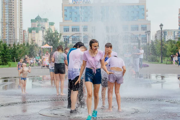 Novokuznetsk, Región de Kemerovo, Rusia - 04 de agosto de 2018: Adolescentes felices salpicando en el agua de una fuente de la ciudad y disfrutando de los frescos arroyos de agua en un día caluroso . — Foto de Stock