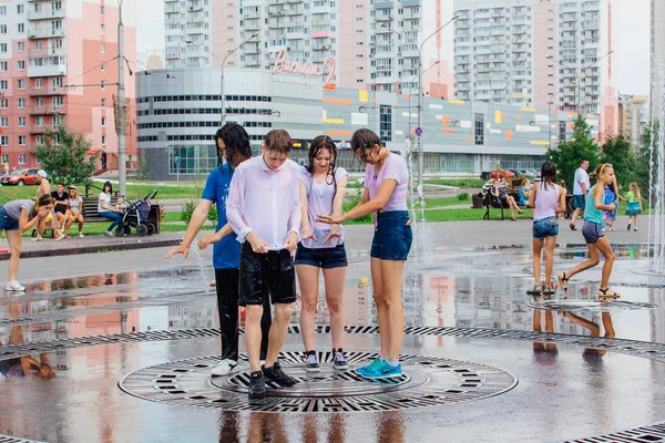 Novokuznetsk, Región de Kemerovo, Rusia - 04 de agosto de 2018: Adolescentes felices salpicando en el agua de una fuente de la ciudad y disfrutando de los frescos arroyos de agua en un día caluroso . — Foto de Stock