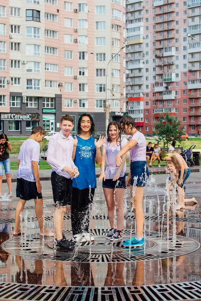 Novokuznetsk, Kemerovo region, Ryssland-Augusti 04, 2018: lyckliga tonåringar stänk i ett vatten i en stad fontän och njuta av den svala strömmar av vatten i en varm dag. — Stockfoto