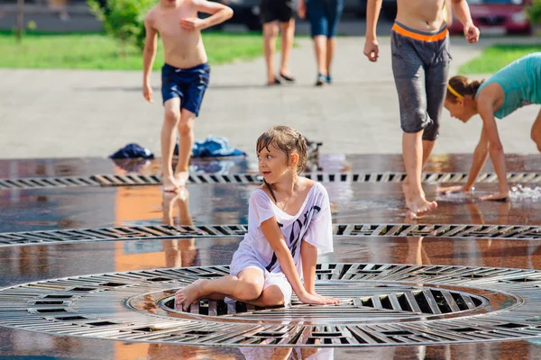 Novokuznetsk, Región de Kemerovo, Rusia - 04 de agosto de 2018: Niños felices salpicando en el agua de una fuente de la ciudad y disfrutando de los frescos arroyos de agua en un día caluroso . — Foto de Stock