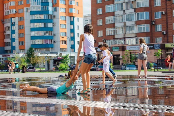 Novokuznetsk, Región de Kemerovo, Rusia - 04 de agosto de 2018: Niños felices salpicando en el agua de una fuente de la ciudad y disfrutando de los frescos arroyos de agua en un día caluroso . — Foto de Stock