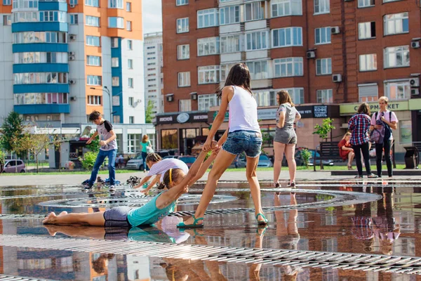 Novokuznetsk, Región de Kemerovo, Rusia - 04 de agosto de 2018: Niños felices salpicando en el agua de una fuente de la ciudad y disfrutando de los frescos arroyos de agua en un día caluroso . — Foto de Stock