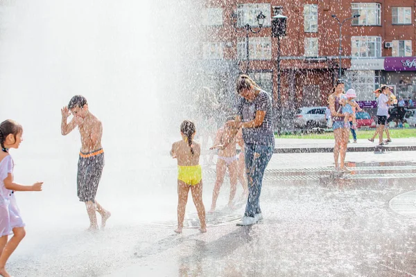 Novokuznetsk, Kemerovo Region, Russia - August 04, 2018: Happy children splashing in a water of a city fountain and enjoying the cool streams of water in a hot day. — Stock Photo, Image