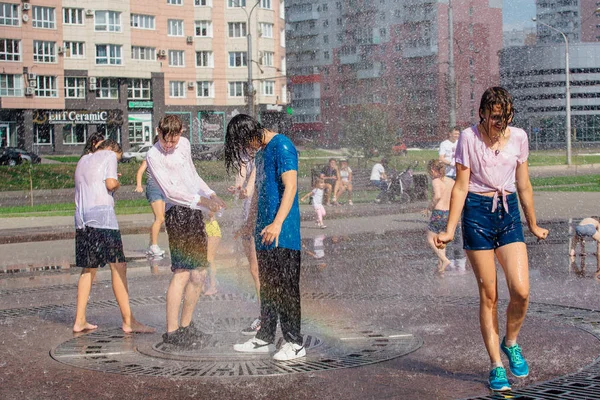 Novokuznetsk, Región de Kemerovo, Rusia - 04 de agosto de 2018: Adolescentes felices salpicando en el agua de una fuente de la ciudad y disfrutando de los frescos arroyos de agua en un día caluroso . — Foto de Stock