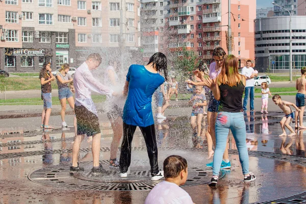 Novokuznetsk, Región de Kemerovo, Rusia - 04 de agosto de 2018: Adolescentes felices salpicando en el agua de una fuente de la ciudad y disfrutando de los frescos arroyos de agua en un día caluroso . — Foto de Stock
