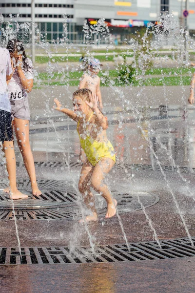 Novokuznetsk, Kemerovo Region, Russia - August 04, 2018: Happy teenagers splashing in a water of a city fountain and enjoying the cool streams of water in a hot day. — Stock Photo, Image