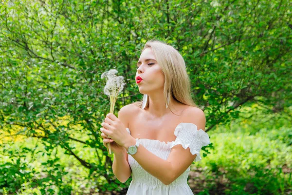 Beautiful blonde woman blowing on white blowball — Stock Photo, Image