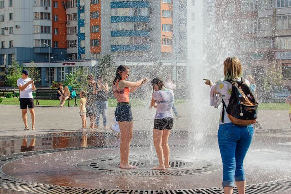 Novokuznetsk, Región de Kemerovo, Rusia - 04 de agosto de 2018: Adolescentes felices salpicando en el agua de una fuente de la ciudad y disfrutando de los frescos arroyos de agua en un día caluroso . — Foto de Stock