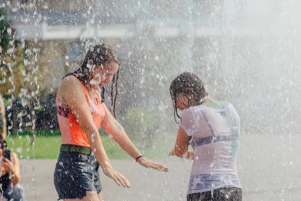 Novokuznetsk, Región de Kemerovo, Rusia - 04 de agosto de 2018: Adolescentes felices salpicando en el agua de una fuente de la ciudad y disfrutando de los frescos arroyos de agua en un día caluroso . — Foto de Stock