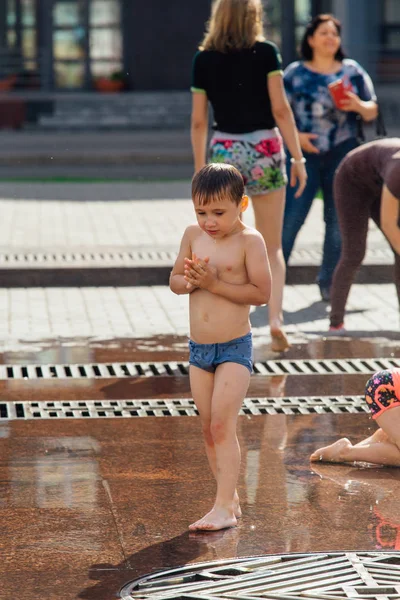 Novokuznetsk, Región de Kemerovo, Rusia - 04 de agosto de 2018: Niños felices salpicando en el agua de una fuente de la ciudad y disfrutando de los frescos arroyos de agua en un día caluroso . — Foto de Stock